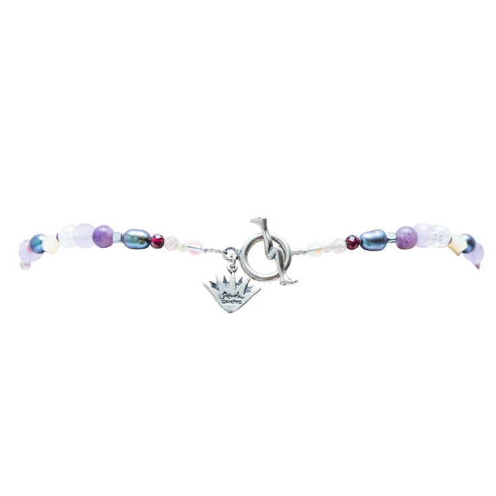 Closure of Handmade Muñeca Mexicana gemstone necklace with purple beads heart accents pearls and silver doll charm on white background