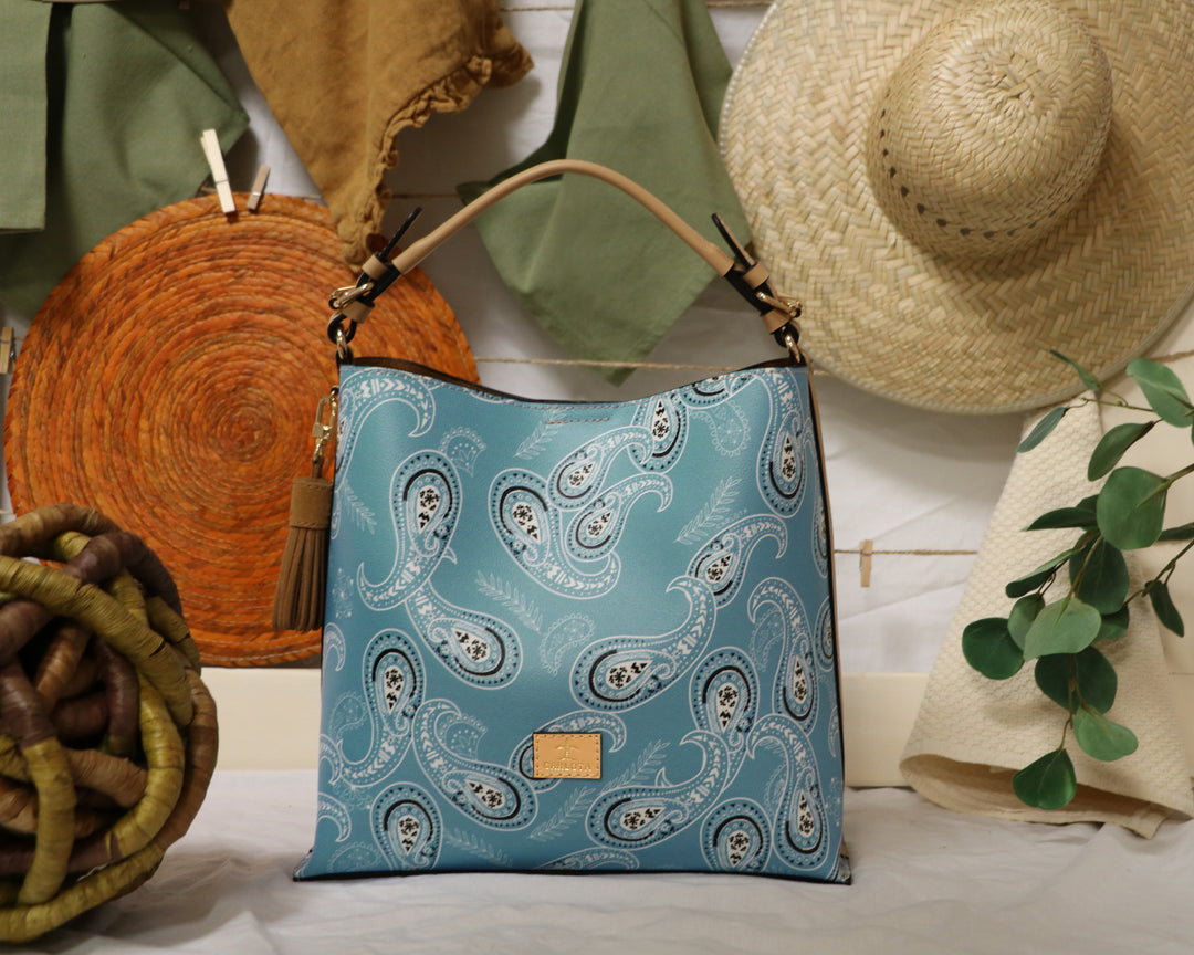 Colorful bandana print leather tote bag styled on linen surface with tassel detail, handmade Mexican handbag Bootsologie