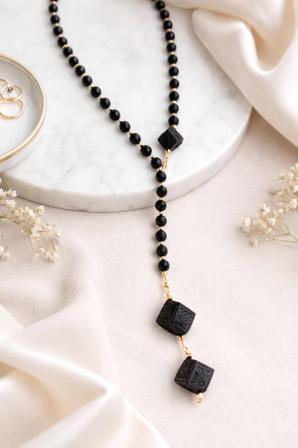 Handmade Barro Negro necklace styled on soft white linen fabric with elegant artisan details, black clay Mexican jewelry by Bootsologie featuring carved Oaxaca ceramic pendants and gold accents.