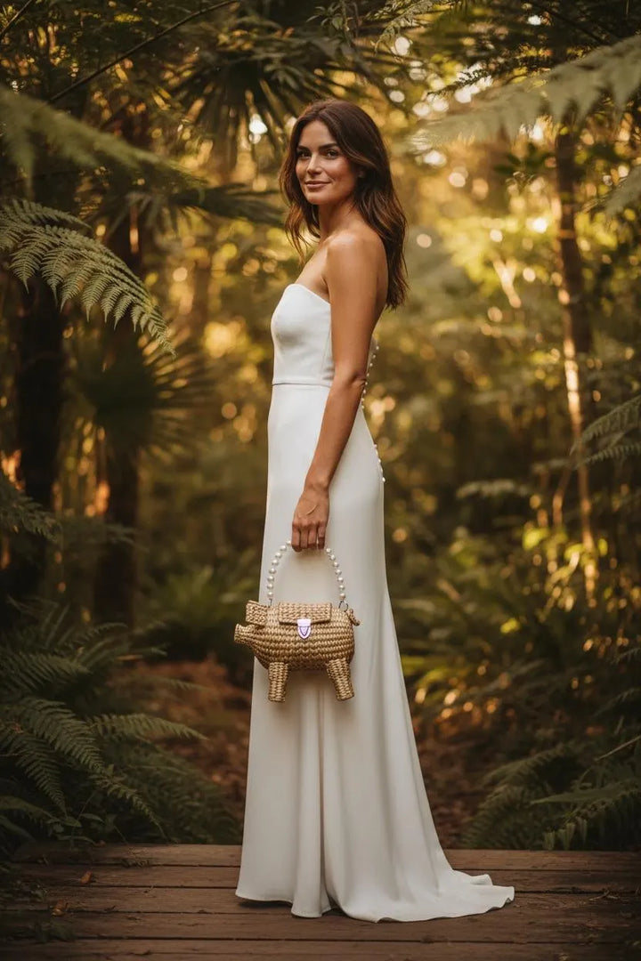 Model wearing elegant formal dress holding pig-shaped straw palm clutch, handmade Mexican evening bag, unique wedding guest accessory