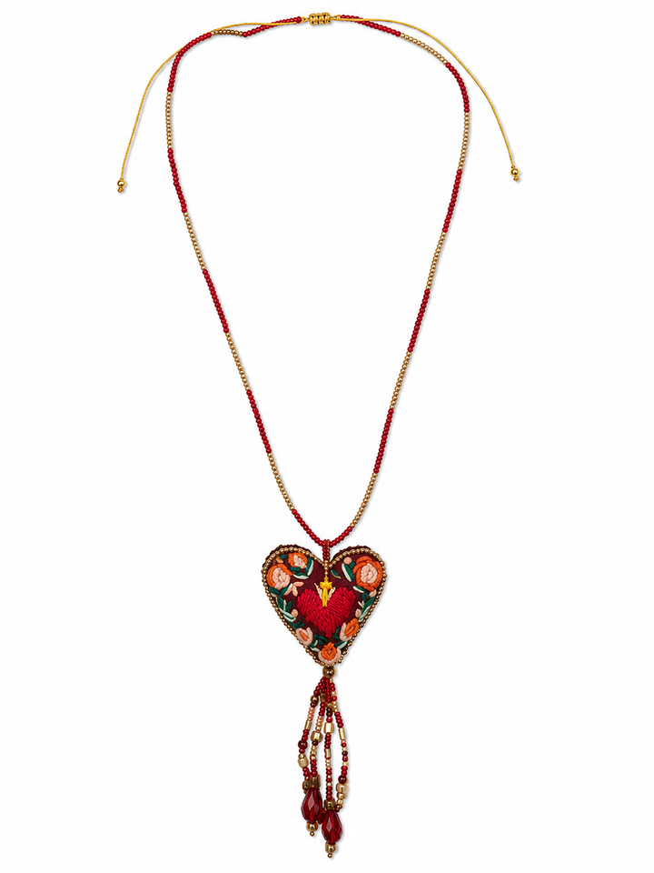 Handmade embroidered sacred heart pendant with ivory tassel and gold bead necklace on white background