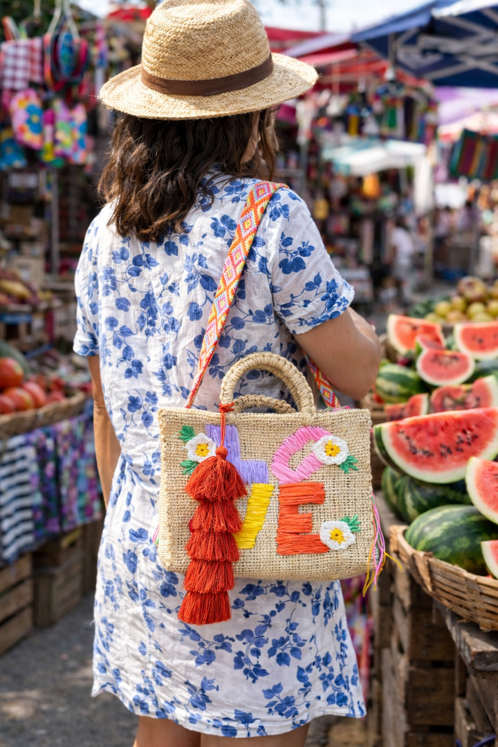 Model wearing a Natural woven Mexican LOVE handbag with floral embroidery, colorful shoulder strap and artisan tassel