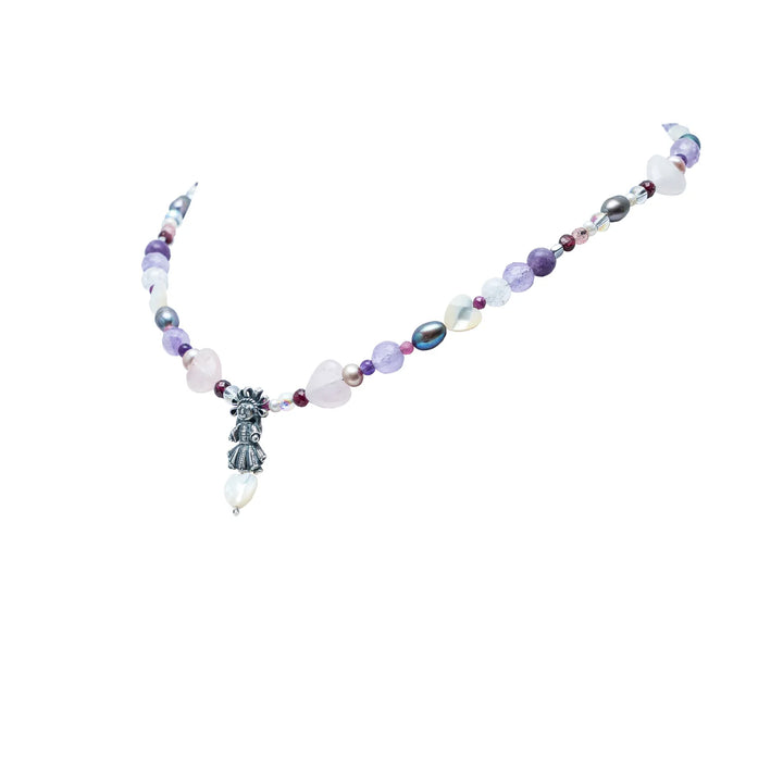 Side of Handmade Muñeca Mexicana gemstone necklace with purple beads heart accents pearls and silver doll charm on white background