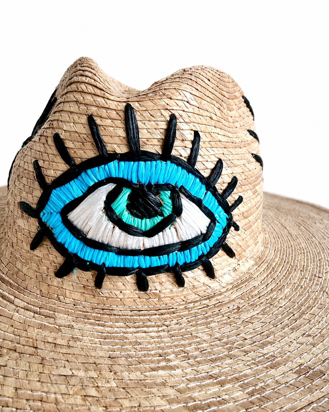 Close-up of embroidered eye motif on natural woven Mexican straw hat