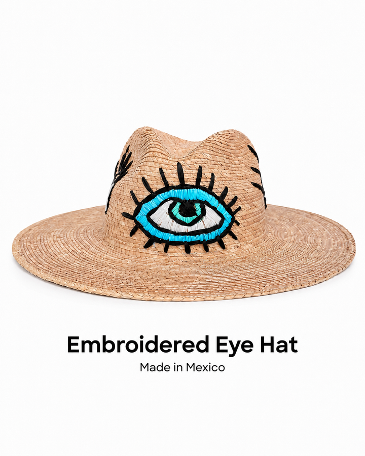 Handmade Mexican straw sun hat with embroidered blue eye motif on white background
