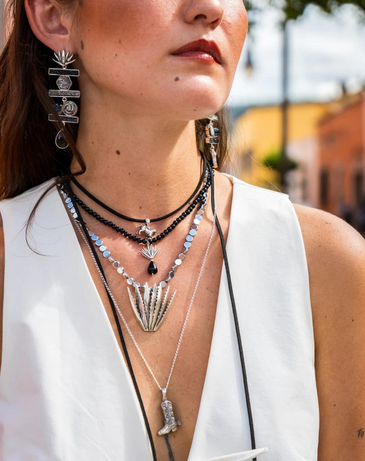 Woman wearing Mexican silver cowboy boot necklace layered with other silver necklaces