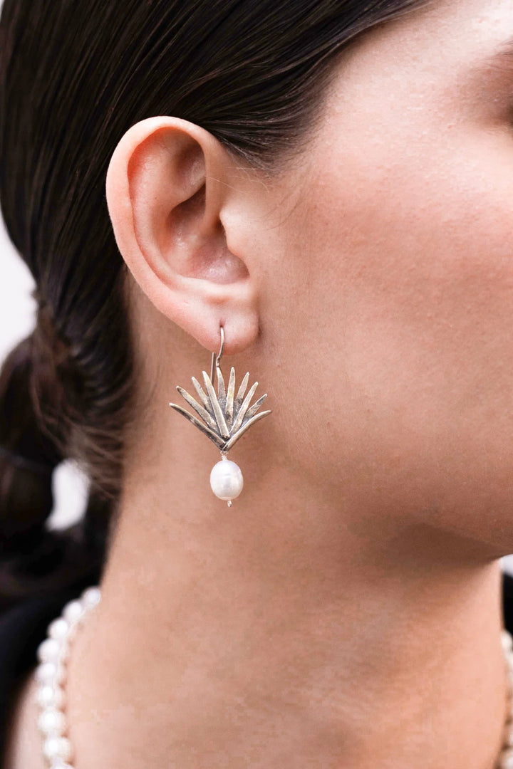 Close-up of a person wearing agave silver earring with a pearl drop.