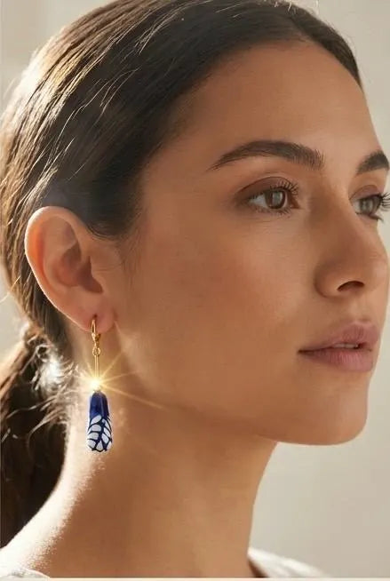 Model wearing Mexican Talavera ceramic dangle earrings with gold plated brass hardware and blue white floral charms
