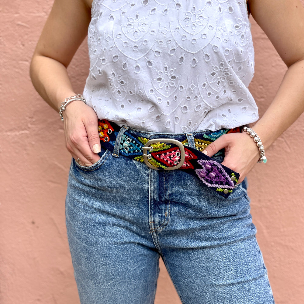 Model wearing navy Peruvian embroidered belt through jean loops with a white blouse for boho everyday style.