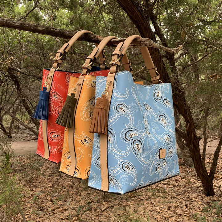 Colorful bandana print leather tote bag styled on linen surface with tassel detail, handmade Mexican handbag Bootsologie